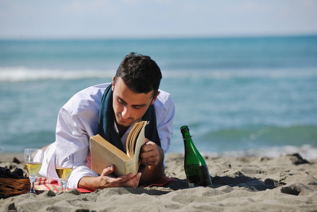 man reading book at beach