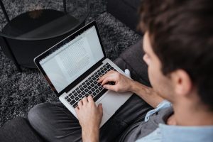 Top view of a concentrated young man working on laptop computer while sitting on sofa at home